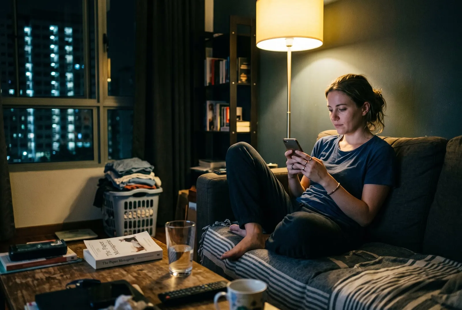 A woman at home on her sofa in the evening, replying to a message on her phone.